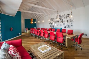 A conference room with red chairs and a wooden table, teal walls, and framed pictures on the wall.