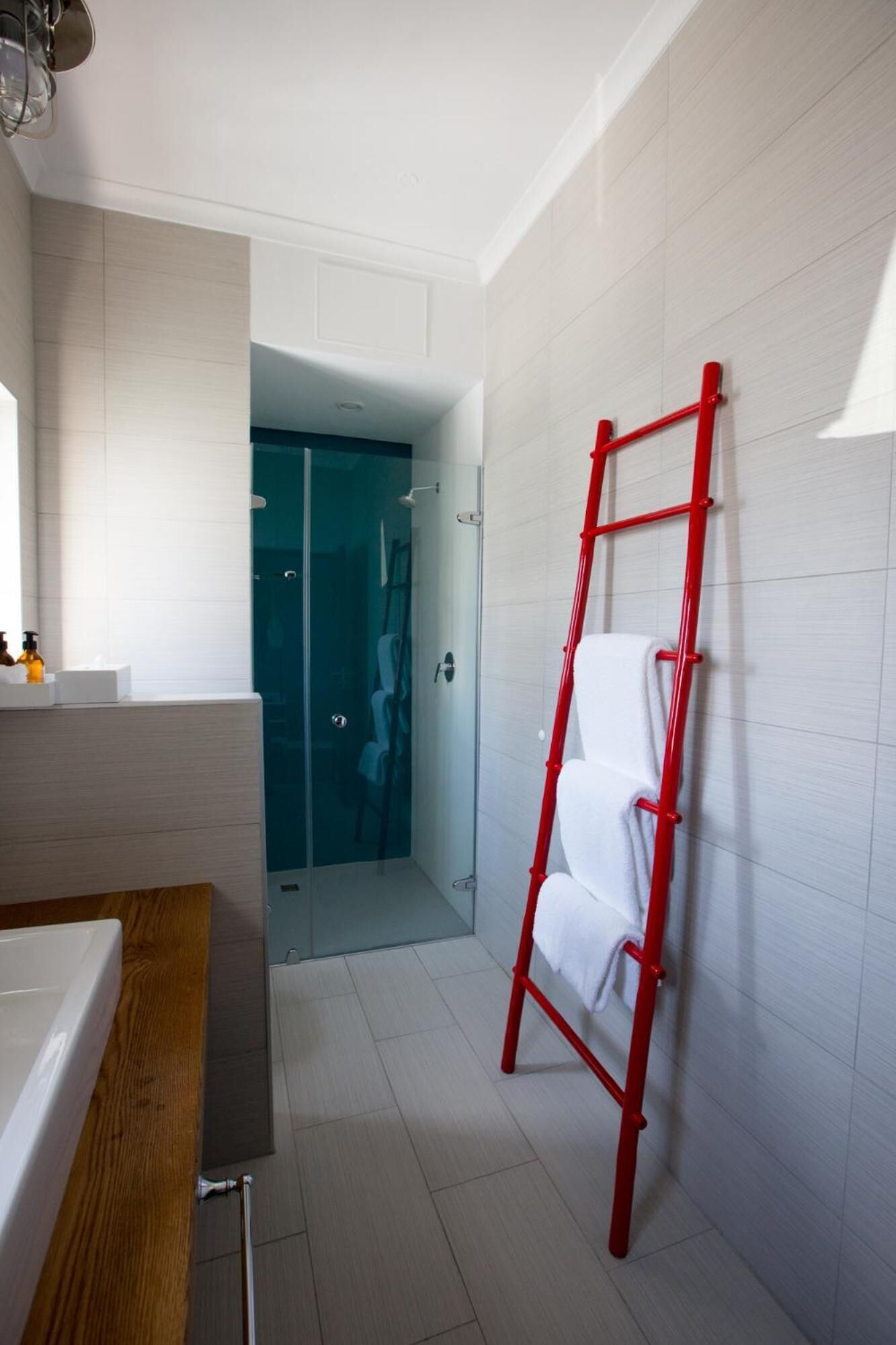 Un baño moderno con una bañera blanca, un tocador de madera, una cabina de ducha de vidrio y una escalera roja apoyada en la pared.