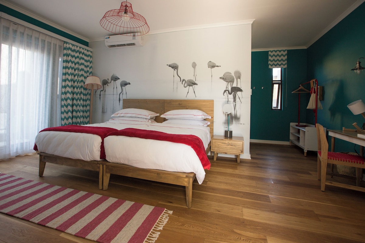 A bedroom with a wooden bed, a red and white striped rug, a wall-mounted air conditioner, and a wall painting of birds.