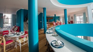 Un intérieur d’hôtel moderne avec un espace de restauration central, de hauts plafonds et des éléments architecturaux bleus distinctifs.