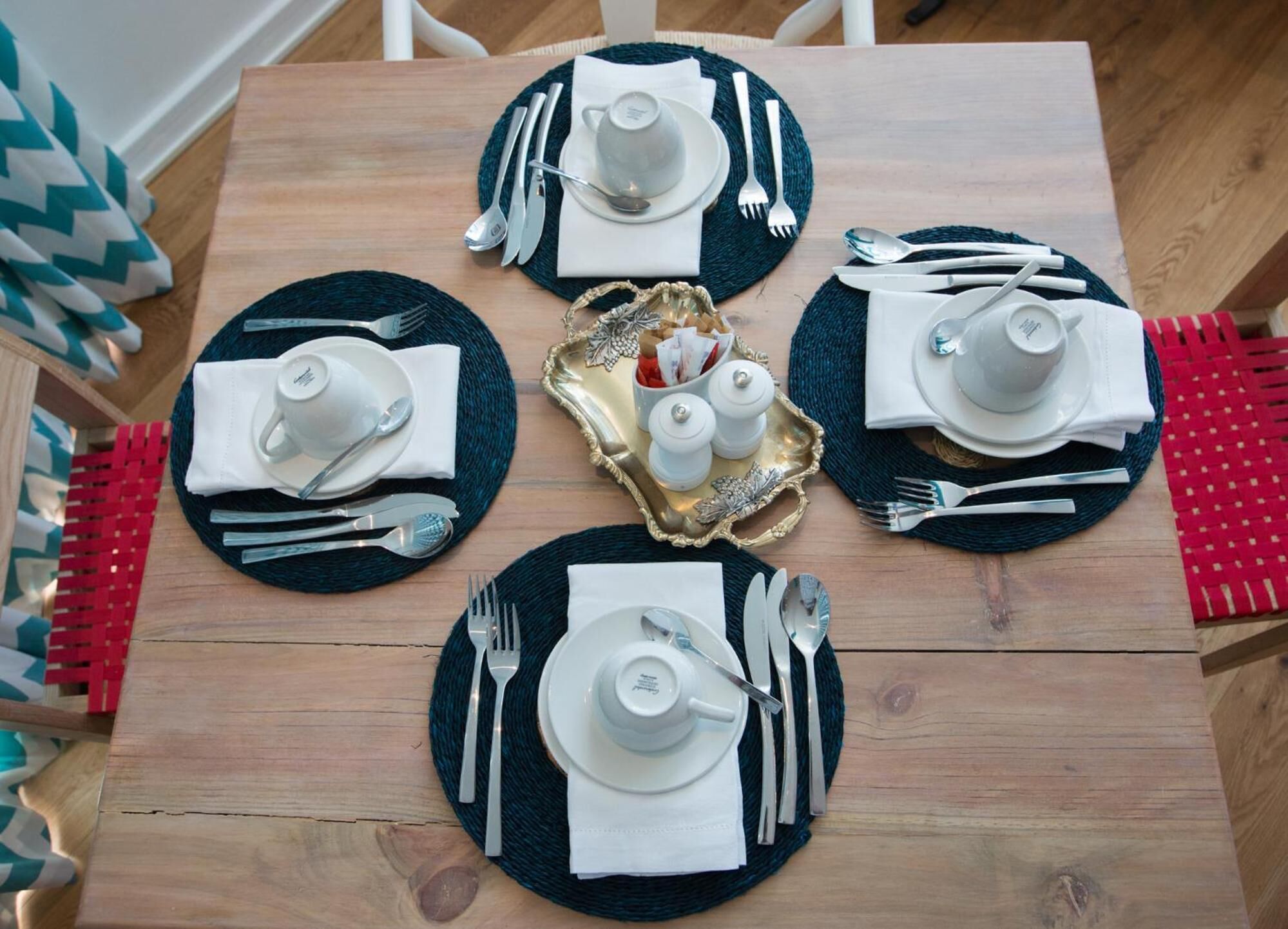 Een houten eettafel gedekt voor vier personen, met zwarte placematen, witte borden en bestek.
