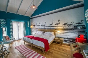 Een slaapkamer met een bed, nachtkastjes, een stoel, een bureau, een rode koffer en een wanddecoratie van flamingo's.