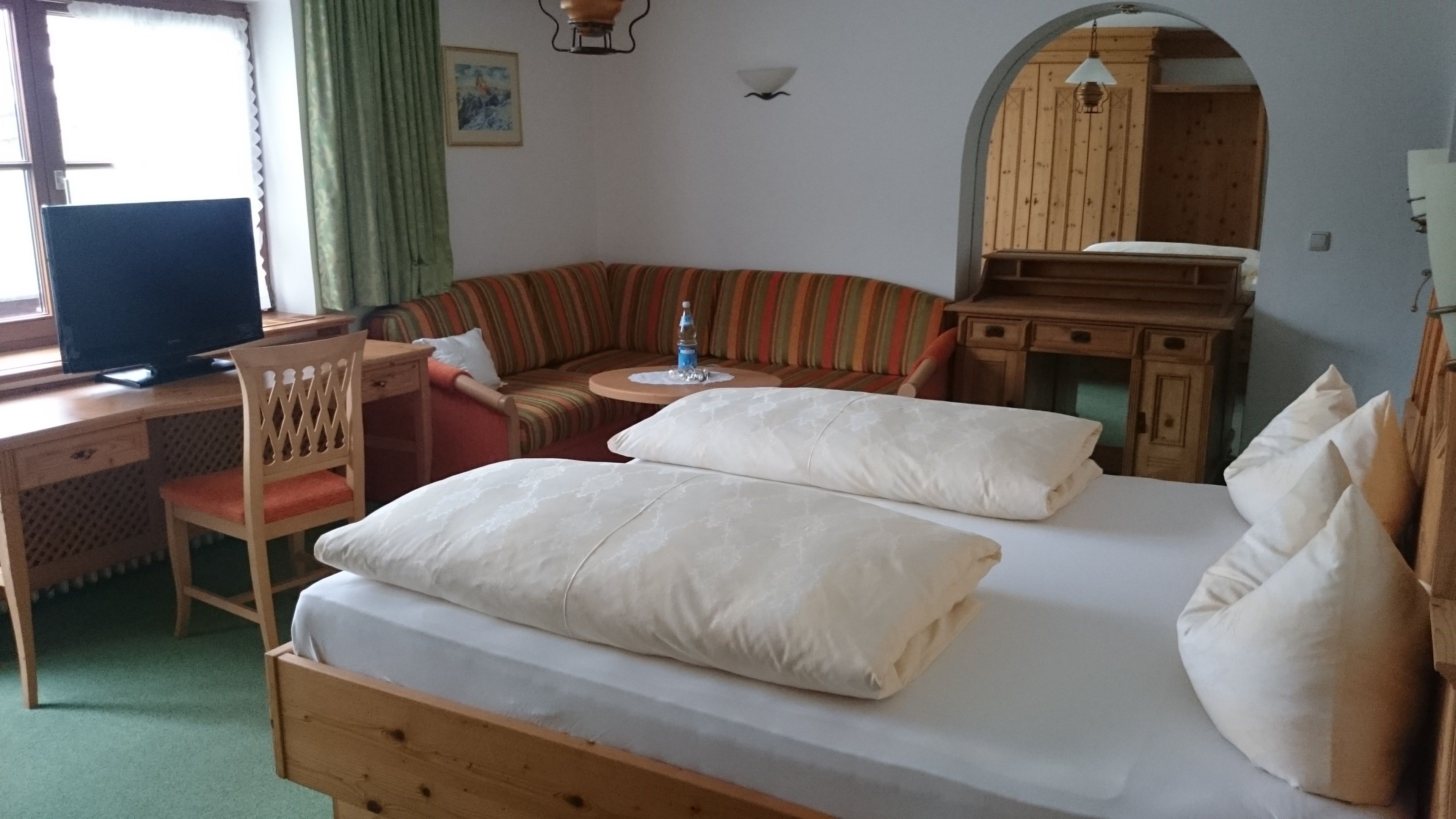 Une pièce confortable avec un lit, un bureau, une chaise, un canapé et une petite table sur laquelle se trouve une bouteille.