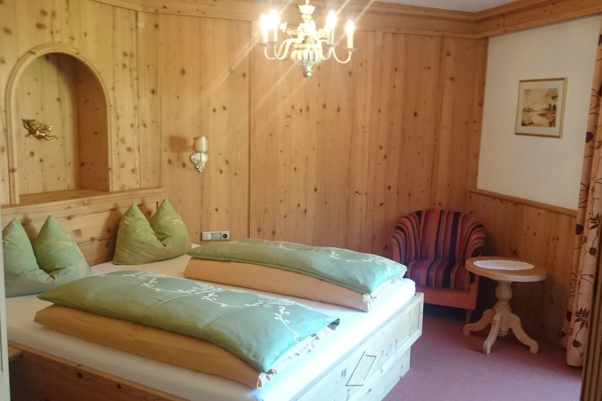Una habitación con paneles de madera, una cama, una silla, una mesita y una araña.