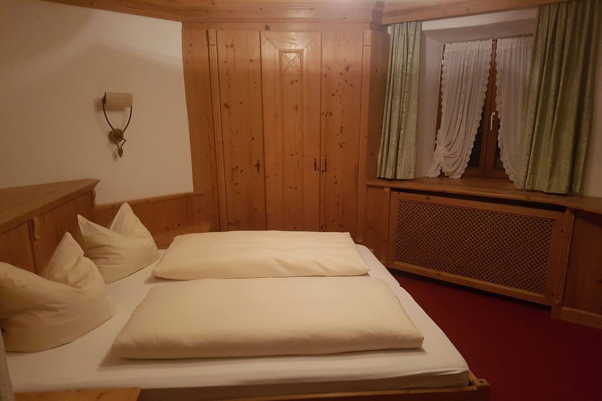 Una cama de madera con ropa de cama blanca en una habitación con paredes de madera y una ventana con cortinas verdes.