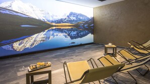 A modern relaxation area with a large wall mural of a mountain lake, comfortable lounge chairs, and a small table with a tray of snacks. - Saint Charles Hôtel & Spa (Val-Cenis)