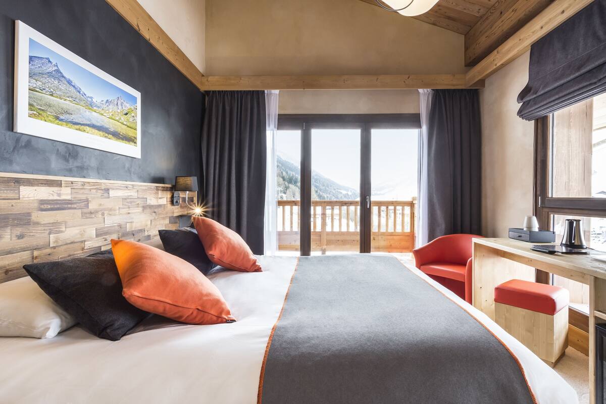 Quarto de hotel com uma cama grande, uma mesa de trabalho e vista para montanhas.