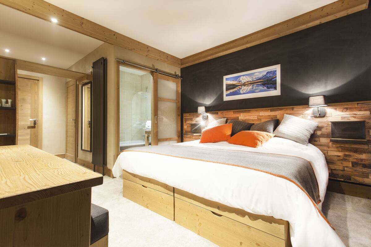 Quarto com cama de madeira, escrivaninha e uma grande janela.
