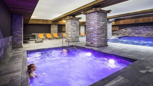 A spa area with a hot tub, stone pillars, wooden beams, and lounge chairs. - Saint Charles Hôtel & Spa (Val-Cenis)