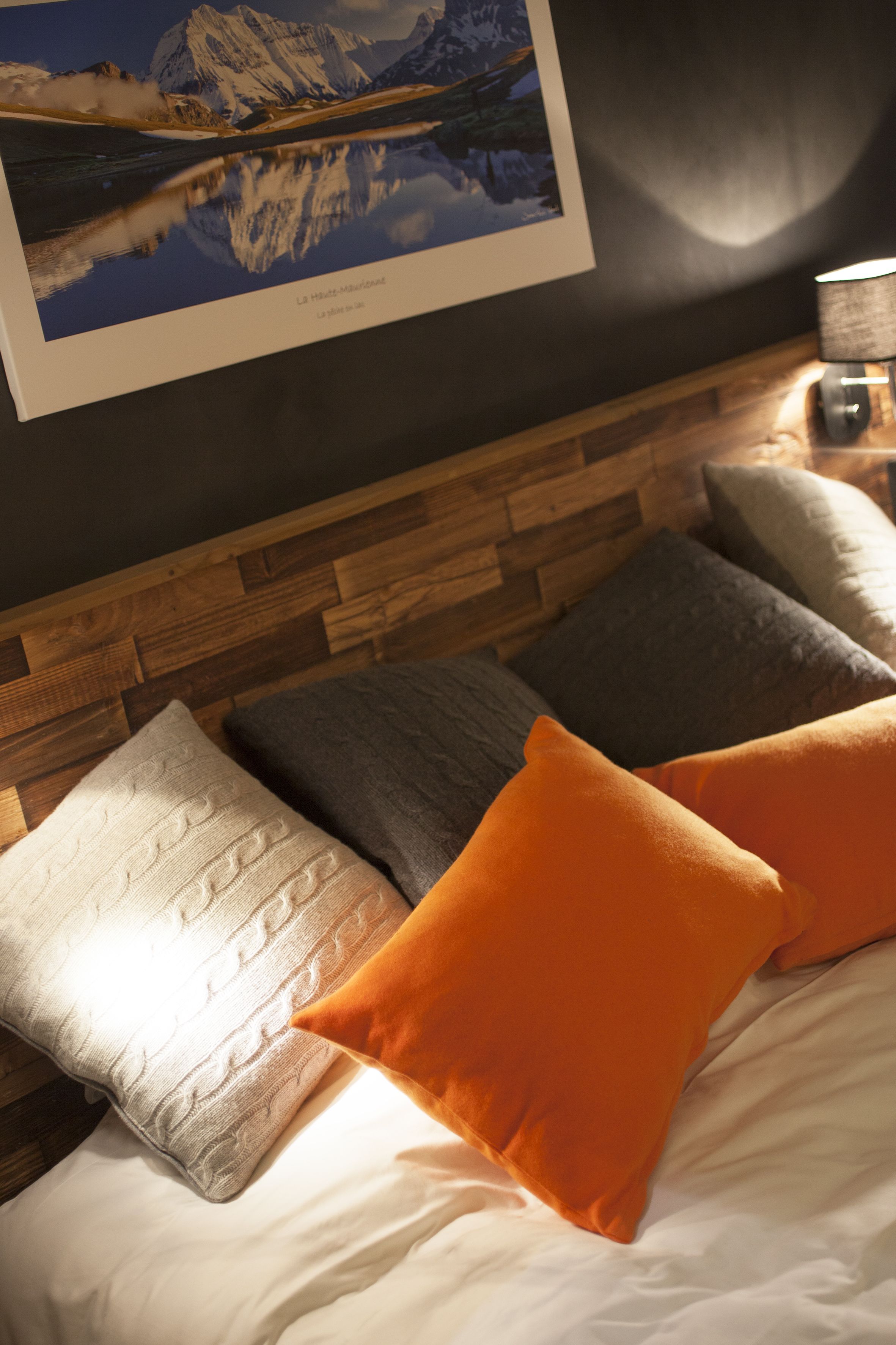 A bedroom with a wooden headboard, a framed landscape painting, and a bedside lamp.
