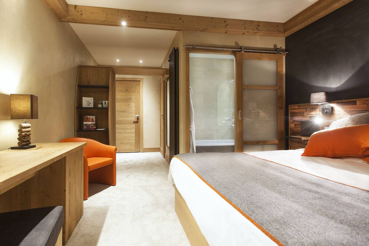 Um quarto com cama, escrivaninha, cadeira e banheiro com chuveiro e vaso sanitário.