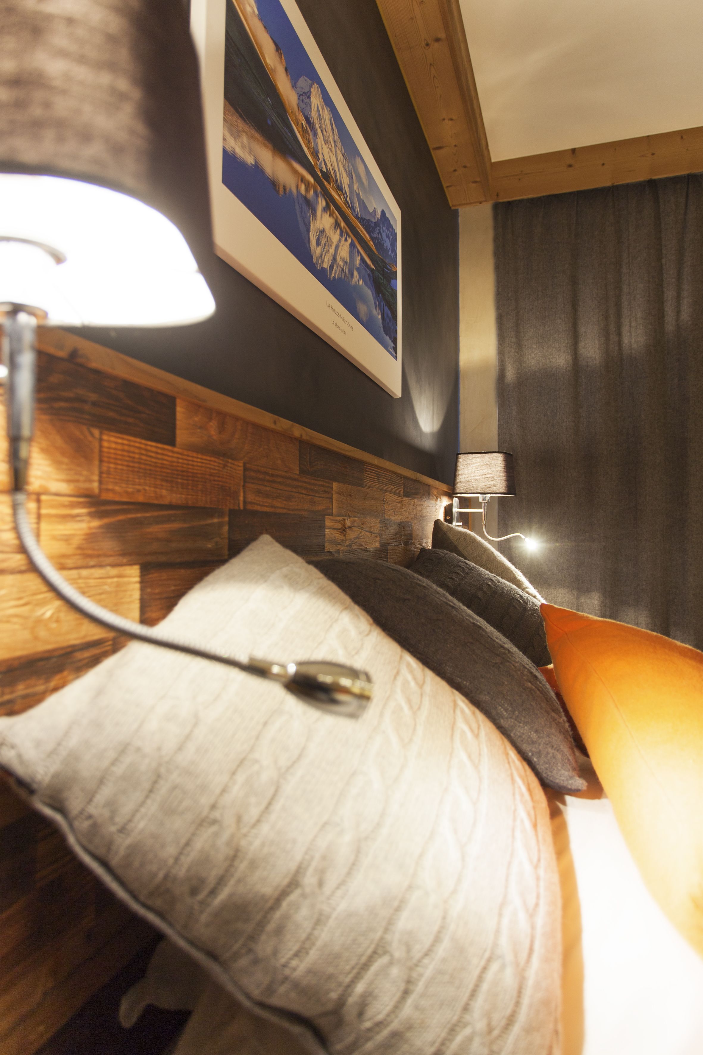 Une chambre d’hôtel avec une tête de lit en bois, un lit doté de plusieurs oreillers, une lampe de chevet et un tableau encadré au mur.