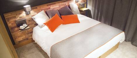 A neatly made bed with a wooden headboard, two bedside lamps, and a small table with cups and a book.