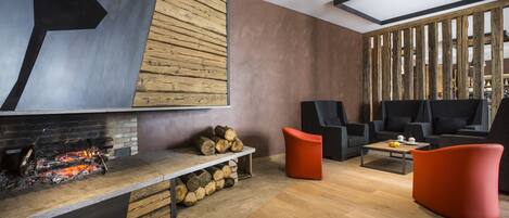 A modern living area with a fireplace, wooden logs, a coffee table, and two red chairs.