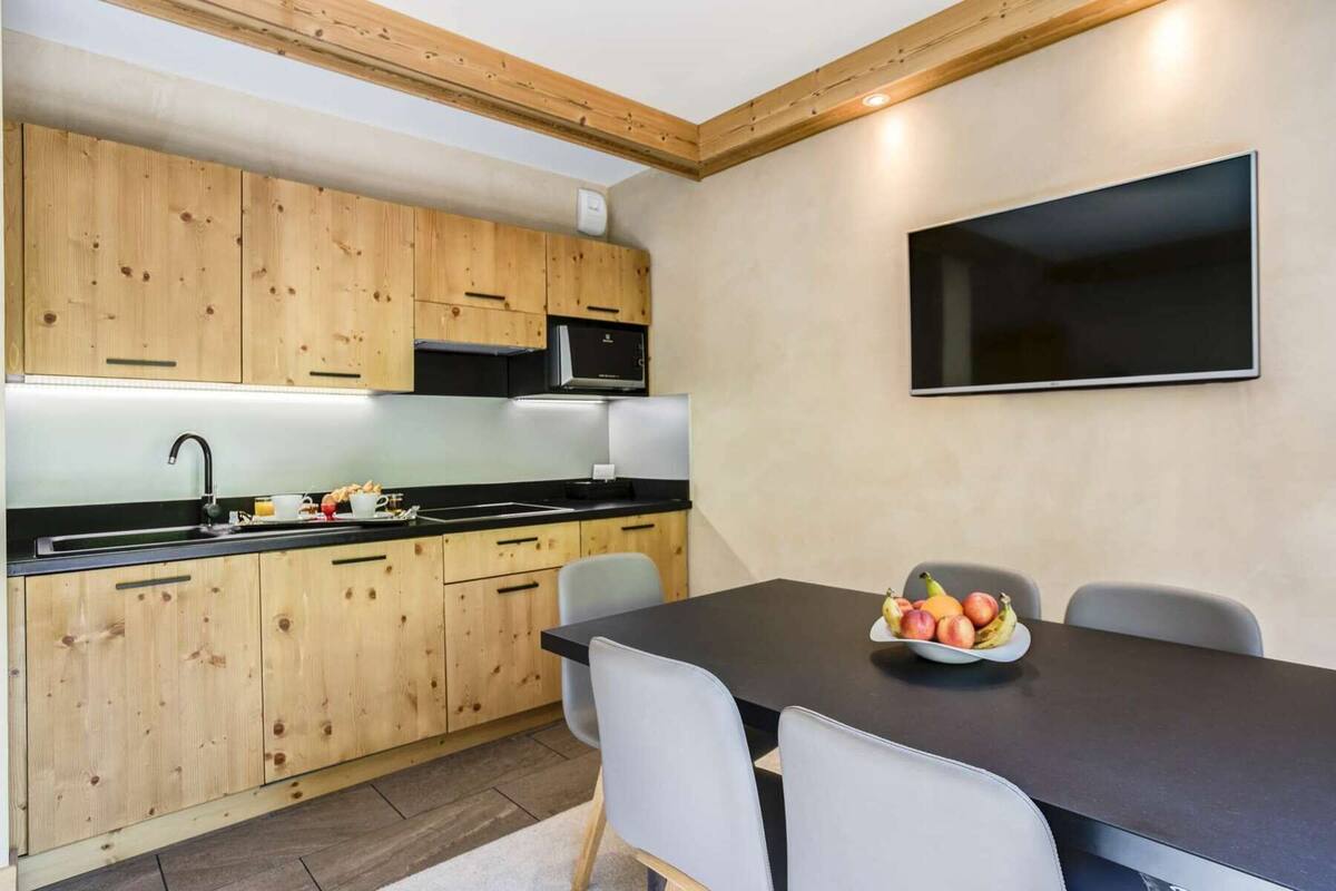 Cozinha moderna com armários de madeira, bancada preta e área de refeições com mesa e cadeiras.