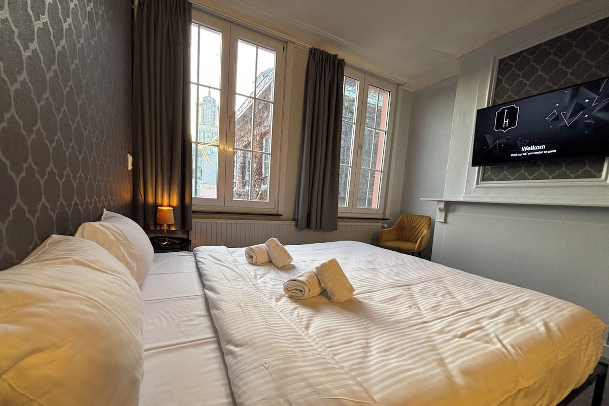Habitación de hotel con dos camas, un televisor en la pared y una ventana con cortinas.