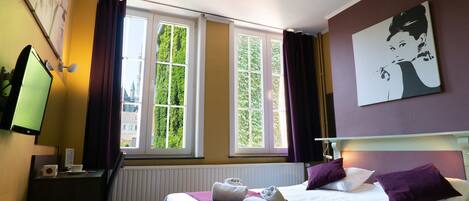 Habitación de hotel con cama, escritorio, silla, televisor y ventana con cortinas.