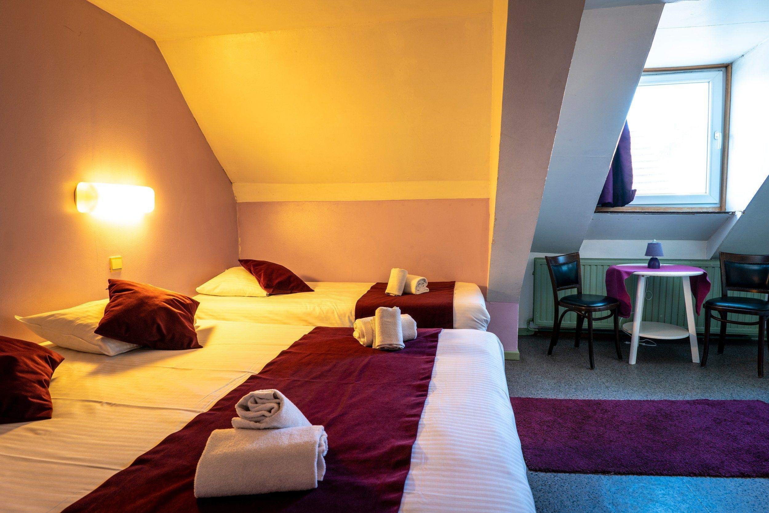 A hotel room with two beds, a small table with chairs, and a window with curtains.