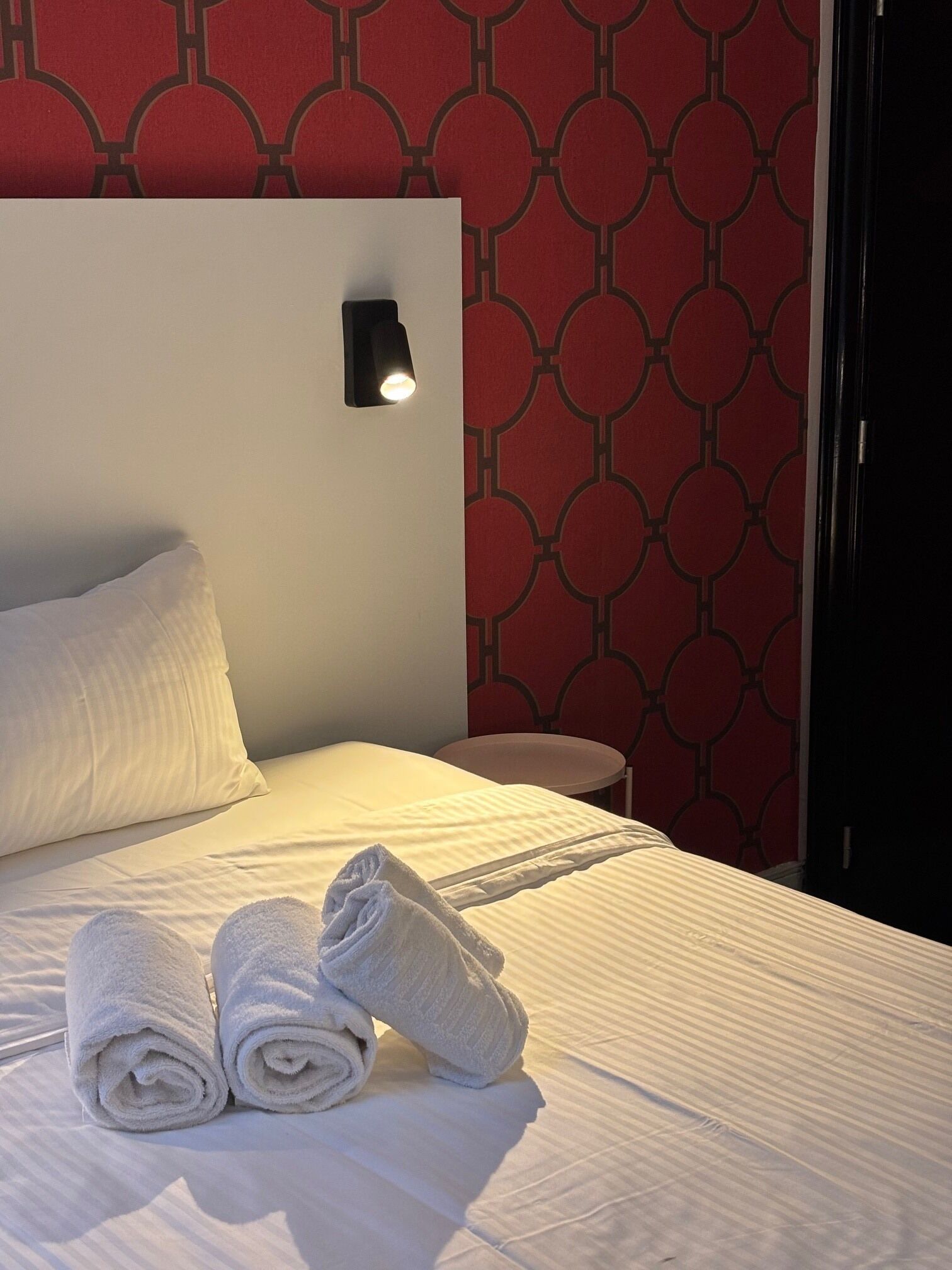 A neatly made bed with rolled white towels, a bedside lamp, and a patterned wall.