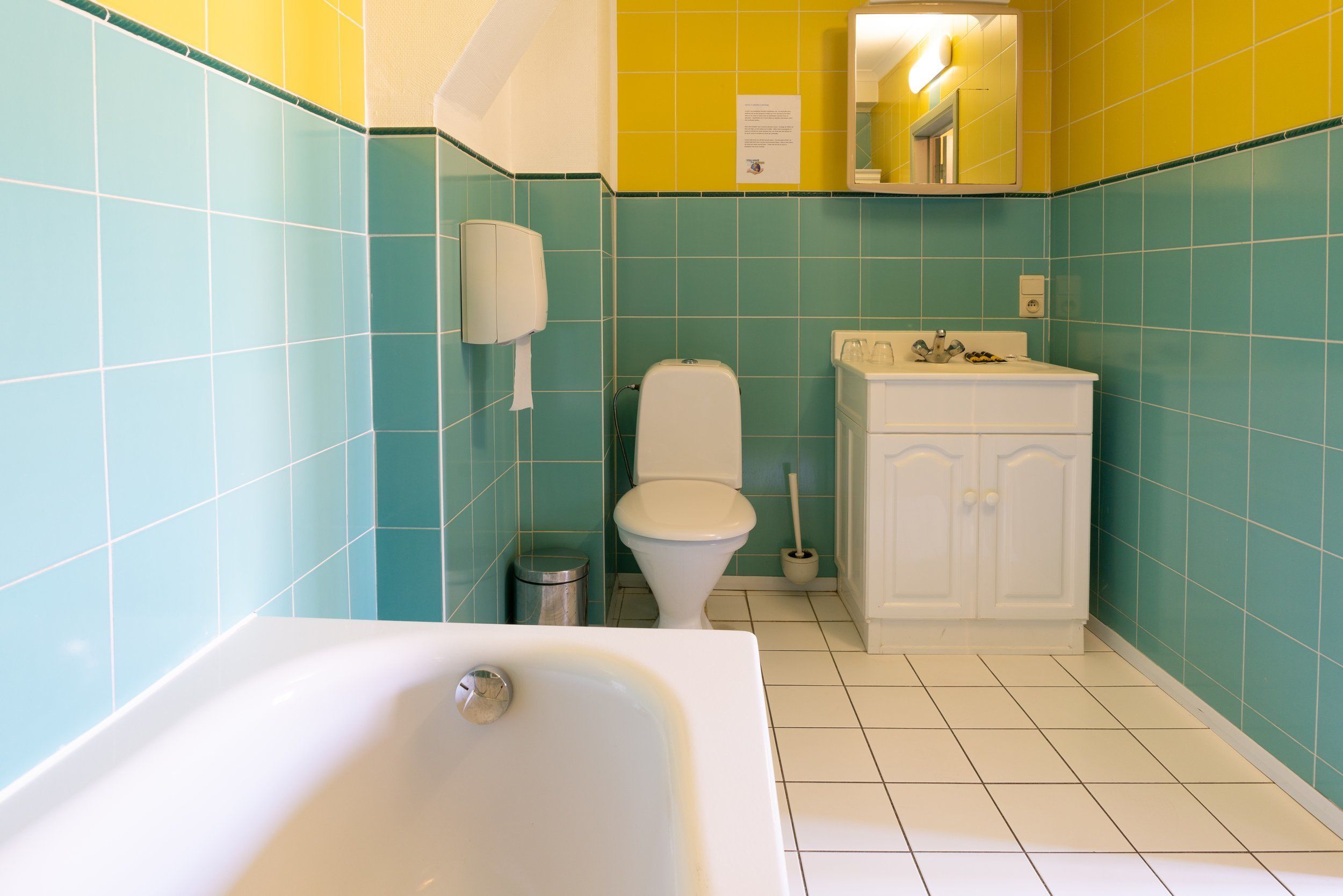 A bathroom with teal and yellow tiles, a white toilet, a white sink, and a white bathtub.