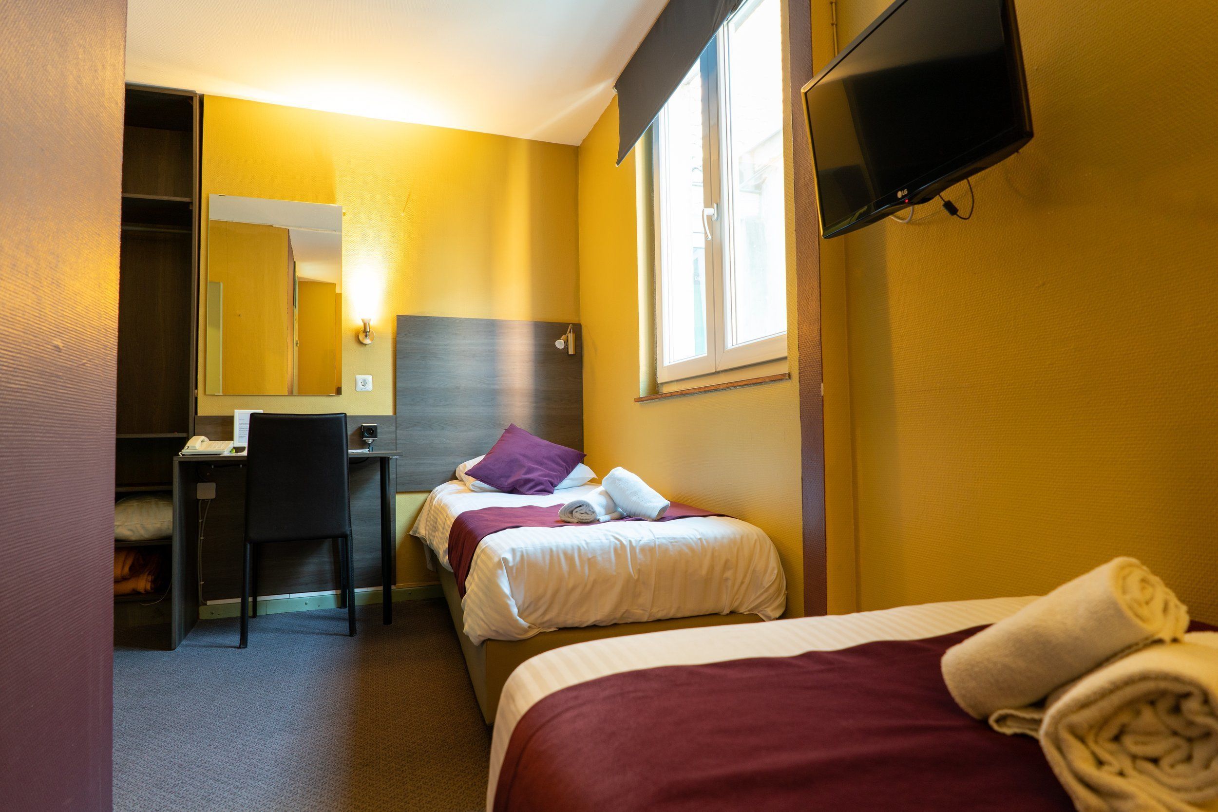 A hotel room with a bed, a desk, a chair, a television, and a window.