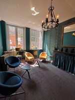 Een kamer met blauwgroene wanden, een kroonluchter, twee fauteuils, een tafel en een spiegel.