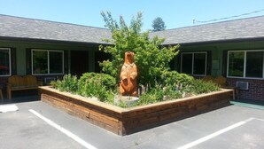 A building with a central garden area featuring a wooden bear sculpture, surrounded by various plants and flowers. - Mingo Motel (Wallowa)