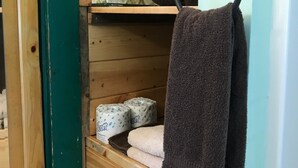 A wooden interior with a towel rack holding two towels, a shelf with toilet paper, and a door with a green frame. - Mingo Motel (Wallowa)