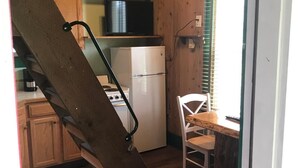 A compact kitchen with a wooden staircase, a white refrigerator, and a dining area with a table and chair. - Mingo Motel (Wallowa)