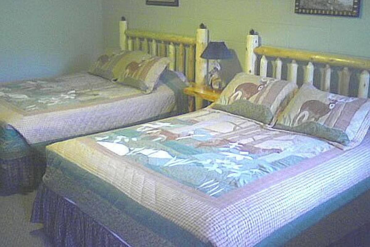 A room with two single beds, a nightstand with a lamp, and two framed pictures on the wall.