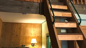 A wooden interior with a lofted sleeping area, a staircase, and a lamp. - Mingo Motel (Wallowa)