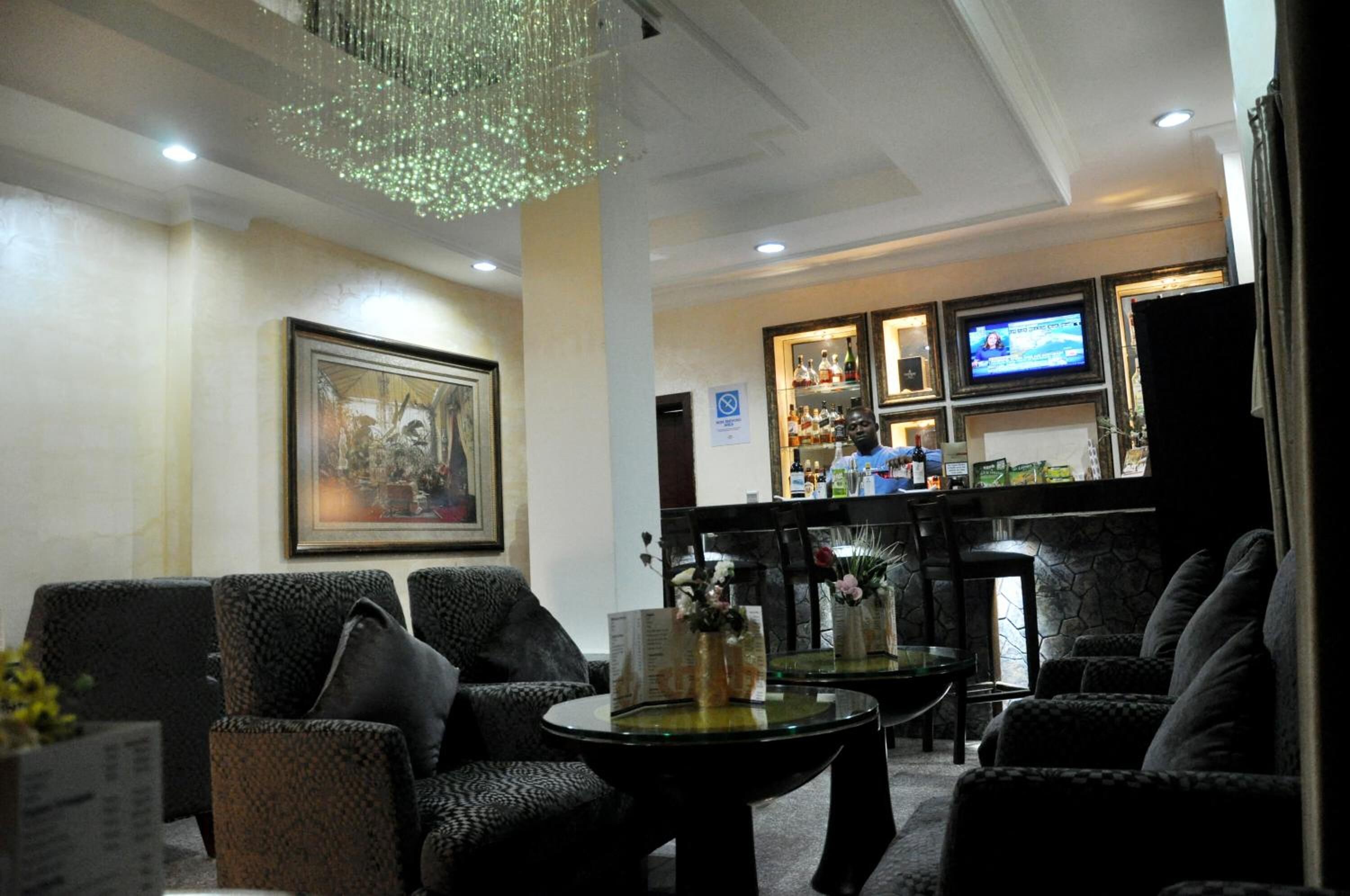 A lobby with dark patterned sofas, a glass coffee table, a chandelier, a bar area with bottles, and a television.