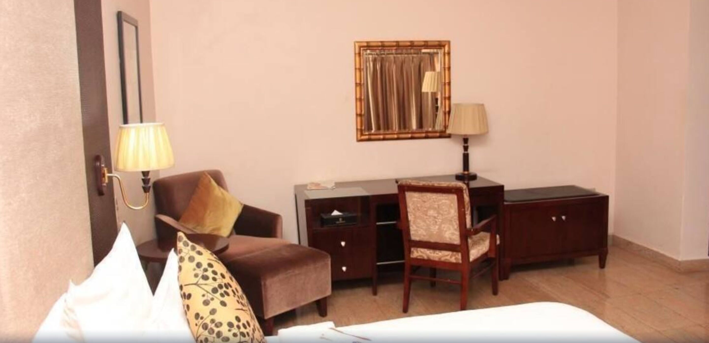 A hotel room with a bed, a desk, a chair, a lamp, a mirror, and a wardrobe.