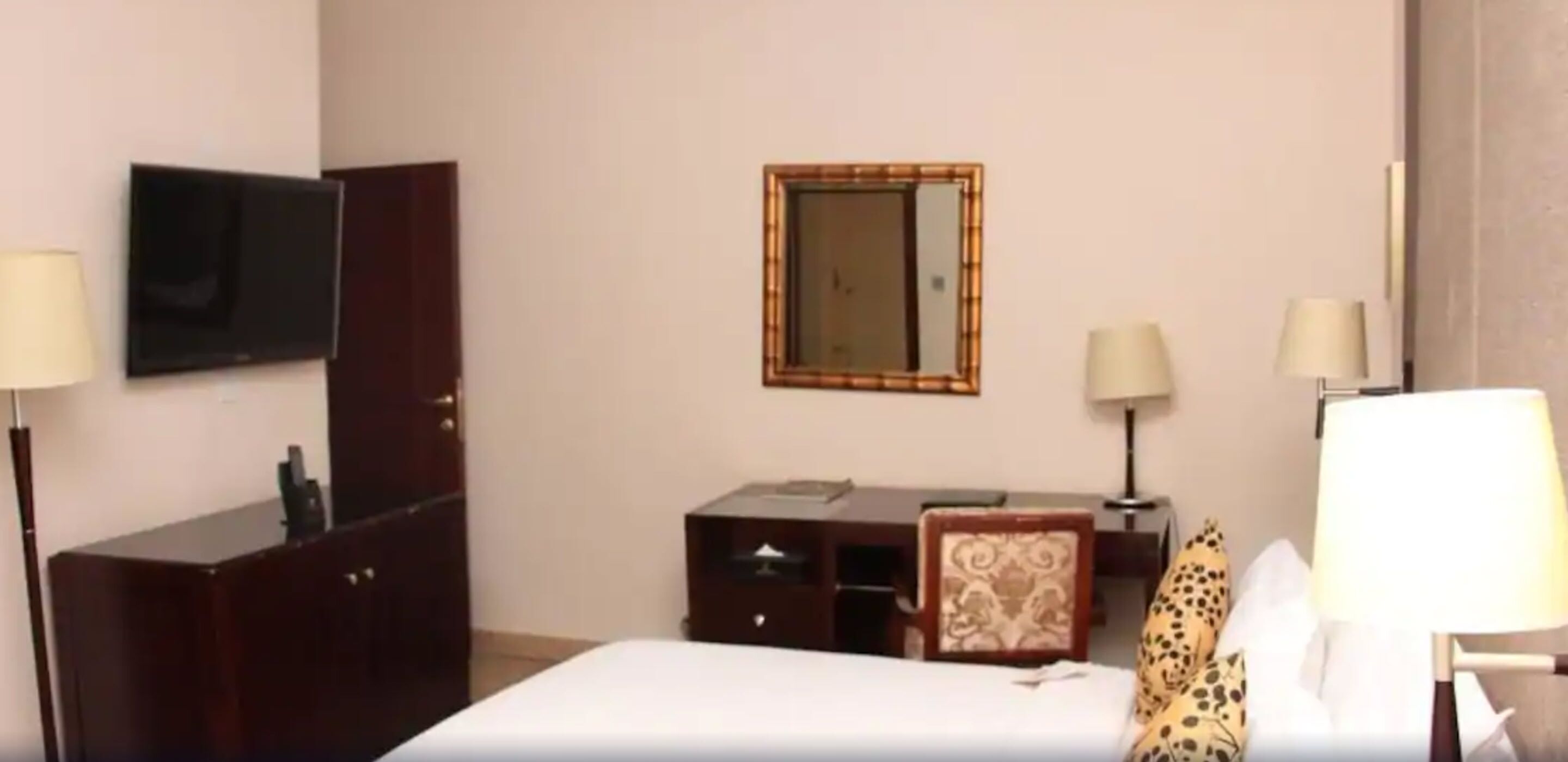Una habitación de hotel con una cama, un escritorio, una silla, un televisor y dos lámparas.