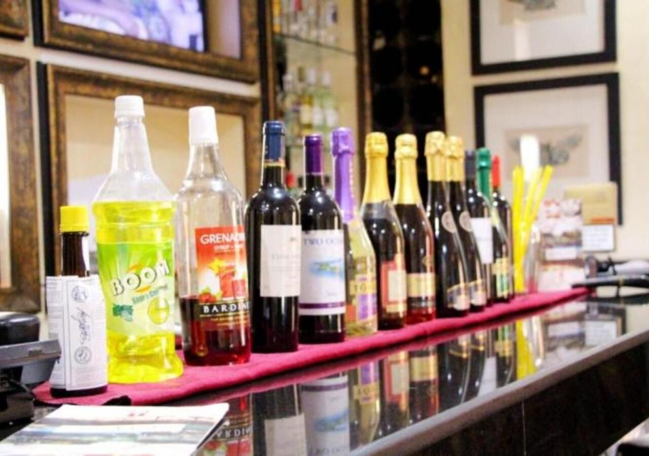 Een barkruk met verschillende flessen alcohol, waaronder wijn en sterke drank, op een roze mat.