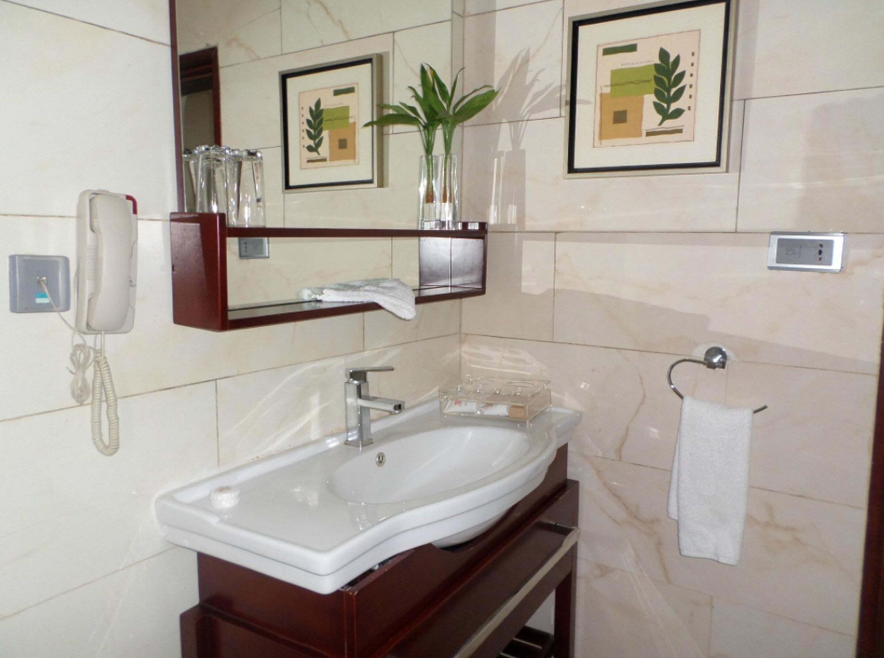 A bathroom with a white sink, a mirror, a telephone, and framed pictures on the wall.