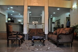 A lobby with a reception desk, two sofas, a coffee table, and a patterned rug. - Hotel Chelsea Wuse 2 (Abuja)