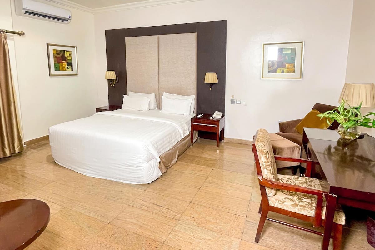 Una habitación de hotel con una cama grande, un escritorio, una silla y una mesita con un florero.