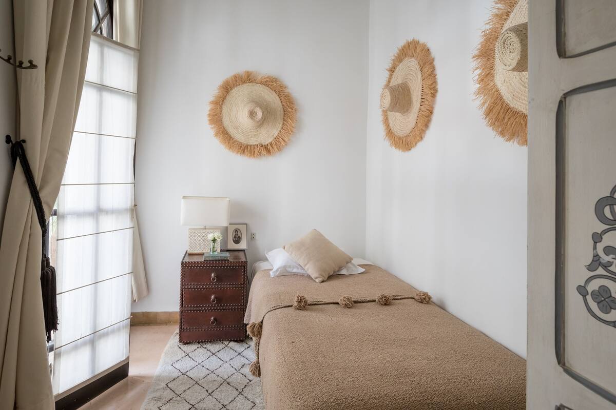 Un dormitorio con cama, cómoda, lámpara y dos sombreros colgados en la pared.