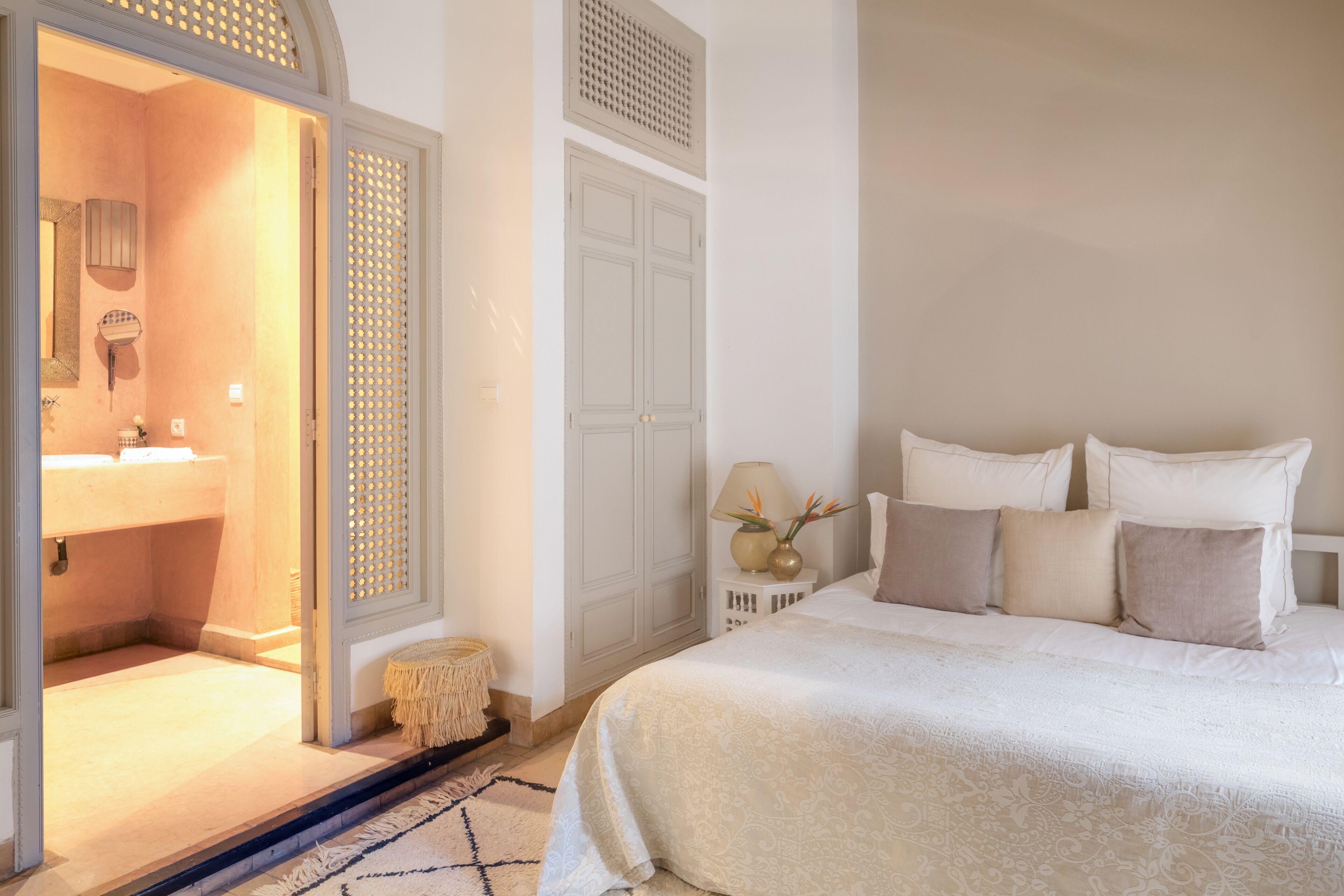 A bedroom with a bed, a nightstand, a lamp, and a door leading to a bathroom.