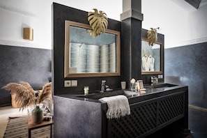 A modern bathroom with a dark marble vanity, a large mirror with a gold leaf design, and a towel rack.