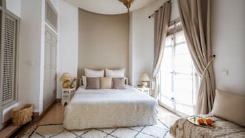 A spacious bedroom with a large bed, a small sofa, and a window with curtains.