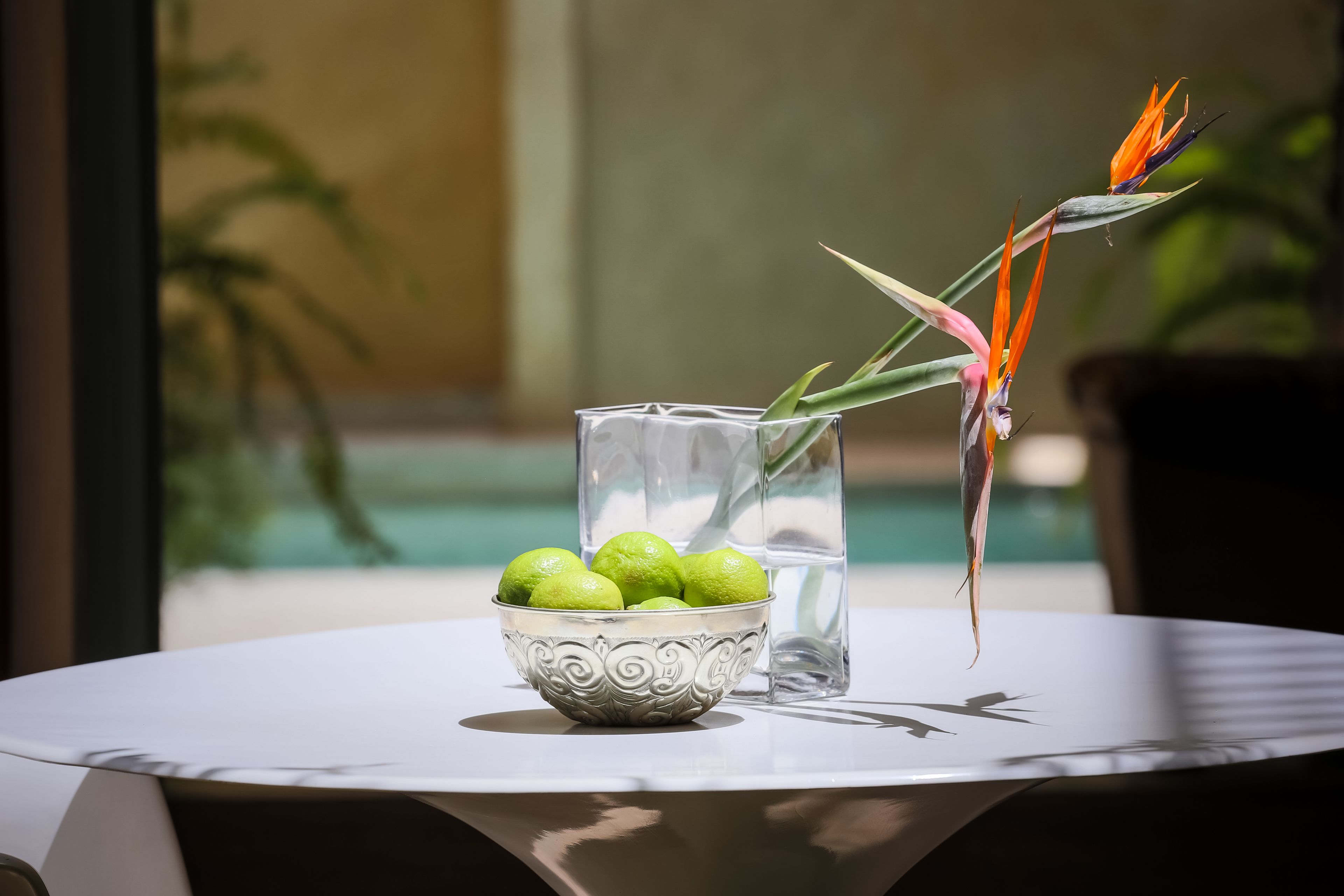 A table with a decorative bowl of green fruits, a clear glass, and a decorative plant.