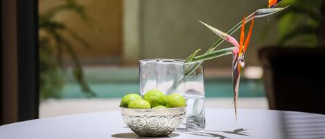 A table with a decorative bowl of green fruits, a clear glass, and a decorative plant.
