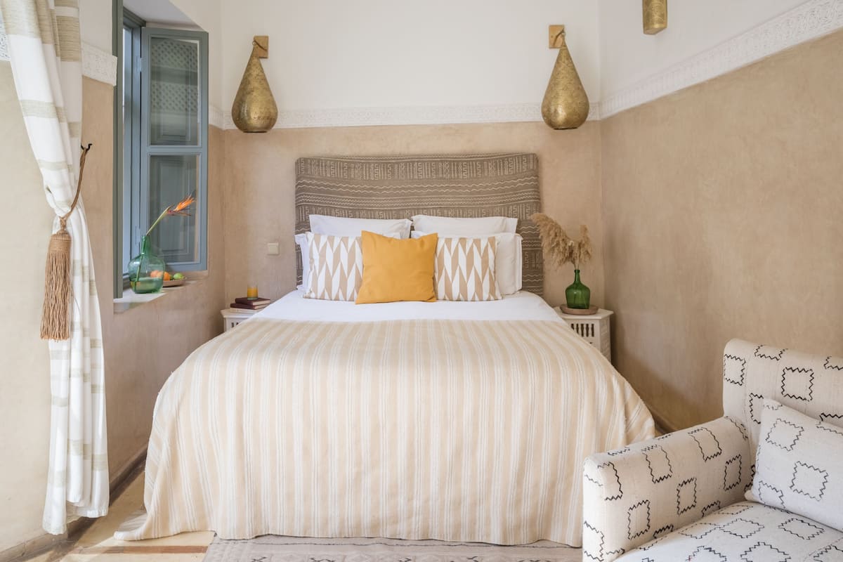 Un dormitorio ordenado con una cama grande, una mesita de noche, una silla y jarrones decorativos.