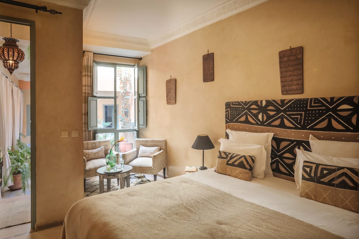 Un dormitorio bien iluminado con una cama grande, cabecera estampada y vistas al exterior a través de una ventana.