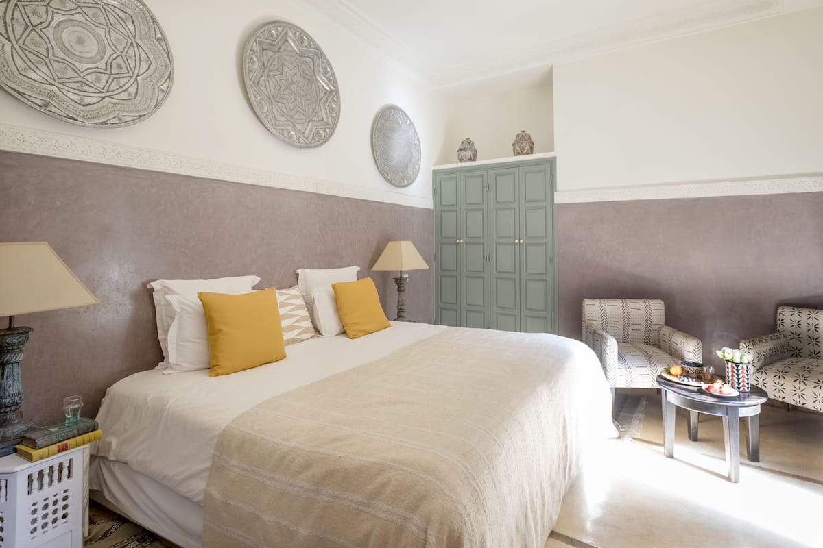 Un dormitorio con una cama, dos mesitas de noche, una silla, un armario y placas decorativas en la pared.