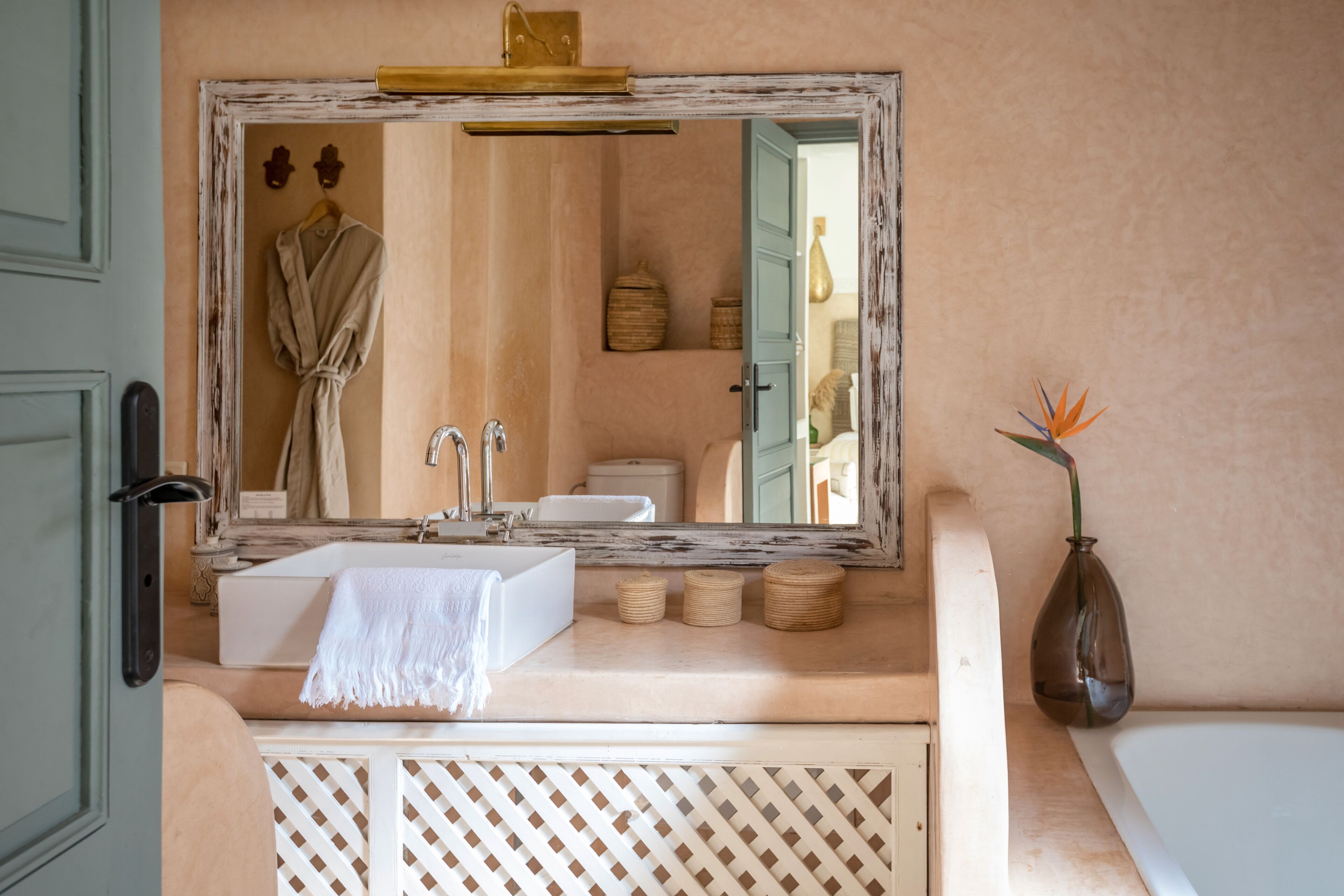 Un baño con un espejo grande, un lavabo blanco, una toalla y un florero con una planta.