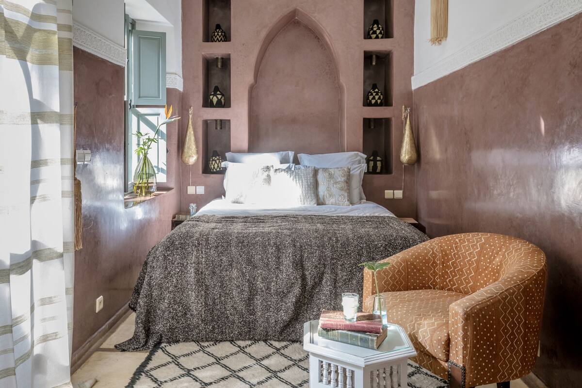 Un dormitorio con una cama, una silla y estantes con adornos.