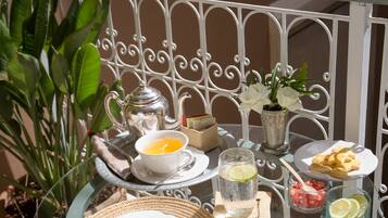Ein Glastisch gedeckt mit einem Teekessel, Tassen, einem Teller mit Essen und einem Blumentopf auf einem Balkon.